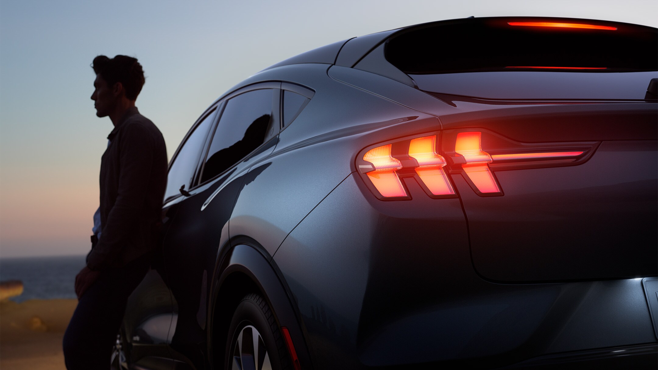 En mand, der læner sig op ad en helt ny Ford Mustang Mach-E ved solnedgang