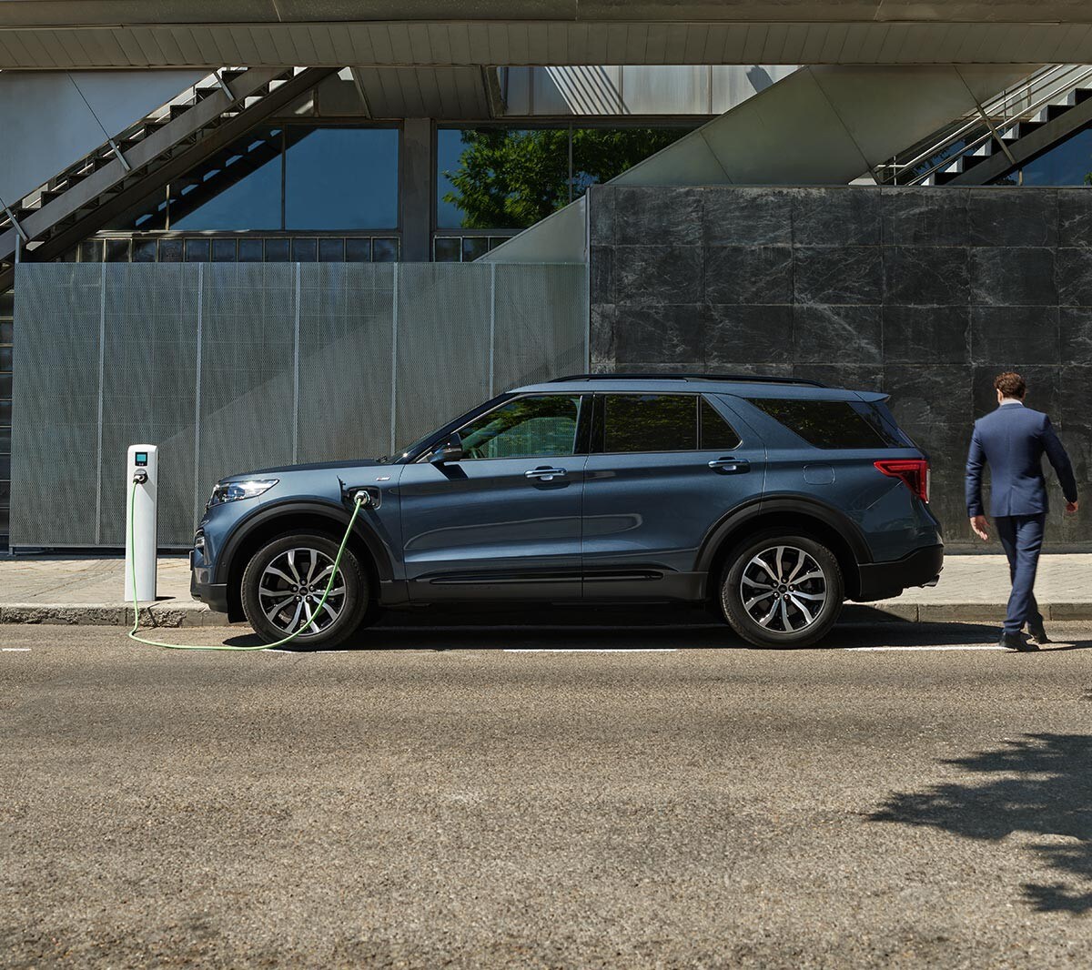 Sidebillede af Ford Explorer PHEV, der holder parkeret ved siden af ​​et ladepunktet med person, der går rundt