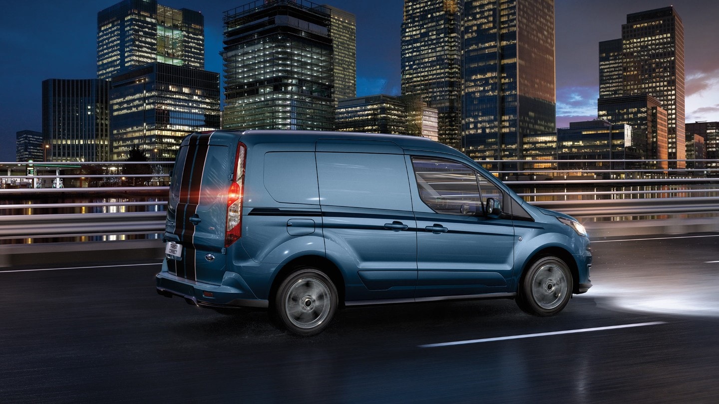Blue Ford Transit Connect Sport driving in the night with headlights on